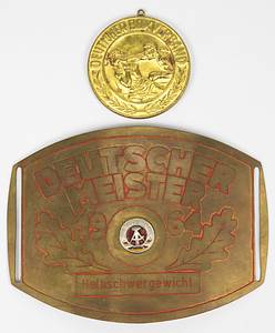 Meistergürtel DDR Boxen 1964  | Original Gürtelschnalle für Bernd Anders (TSC Berlin) den DDR Meister im Boxen mit der Aufschrift "Deutscher Meister 1964 Halbschwergewicht". Messing, mit geröteten Linien und aufgesetztem farbig emaillierten DDR-Staatswappen, 15x11 cm. Dabei die dazugehörige Siegermedaille für den DDR Meister 1964 des Deutschen Boxverbandes mit rückseitiger Gravur "Deutscher Meister 1964 Halbschwergewicht". Bronze, vergoldet mit aufgesetztem emaillierten Staatswappen, 6 cm. - Bild 2