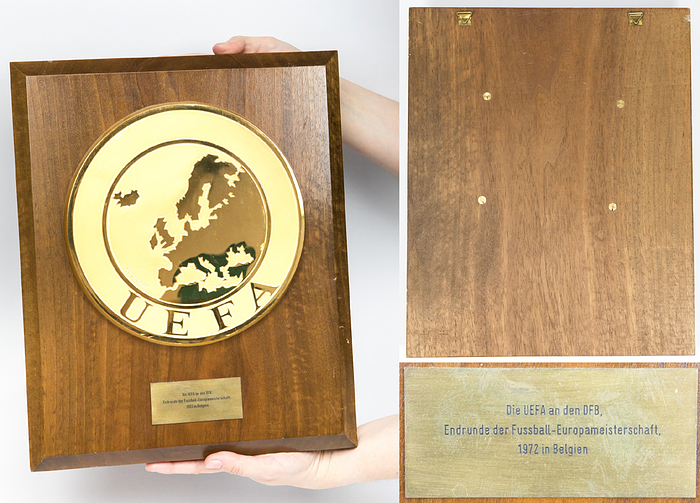 Ehrentafel UEFA Euro 1972  | Große offizielle Teilnehmerplakette für den DFB für die Teilnahme an der Endrunde der UEFA EURO 1972 in Belgien. teilgenommen haben. Jeder teilnehmende Landesverband erhielt eine dieser Plaketten. Holzplatte aus Eichenholz mit aufgeschraubter großem Logo der UEFA. Vergoldete Messingplakette, Hersteller "Huguenin". (21 cm) und aufmontierter gravierter Mesingplakette (8x3,5 cm) mit der Aufschrift  "Die UEFA an den DFB Endrunde der Fussball Europameisterschaft 1972 in Belgien". 35x28,5 cm. Unikat. Museumstück!.