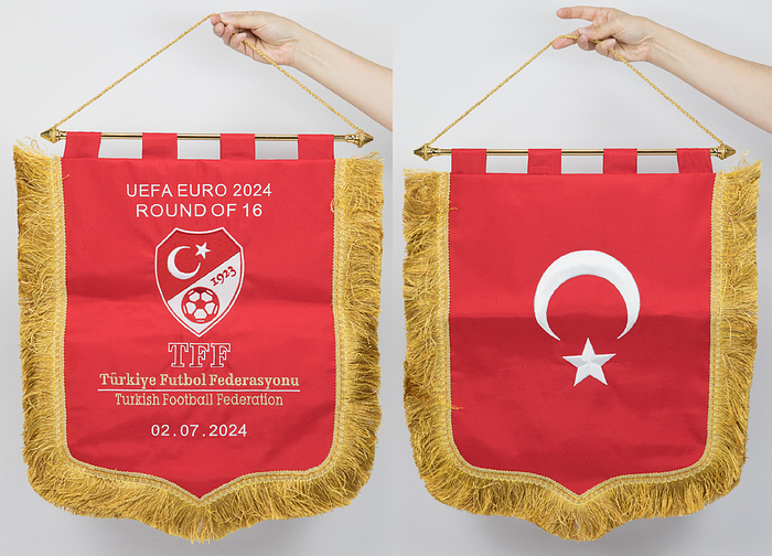  - Turkey's official match pennant for the UEFA Euro 2024 match on July 2, 2024, against Austria (2-1) in Leipzig. Featuring the embroidered lettering "UEFA EURO 2024 Round of 16. Turkish Football Federation 02.07.2024." Featuring the embroidered Turkish Football Federation logo. Reverse features the Turkish national flag. Silk pennant with white silk fringes, metal pole with gold-plated balls. 55 x 48 cm. --This pennant is the original exchange pennant, which was handed over by the Turkish captain to the Austrian captain! It came from the collection of an official of the Austrian Football Association, who took the pennant at the start of the game and was allowed to keep it! Condition: A