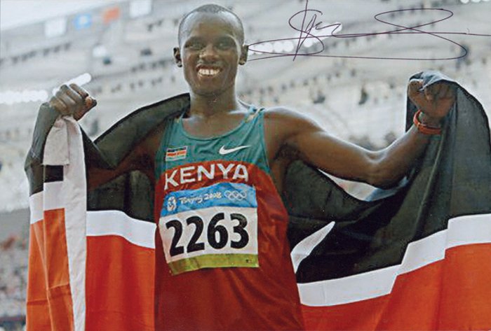 Wanjiru, Samuel Kamau  | (1986-2011) Farbreprofoto mit original Signatur von Samuel Kamau Wanjiru (KEN). Goldmedaille im Marathon bei den Olympischen Spielen 2008. 15x10,5 cm.