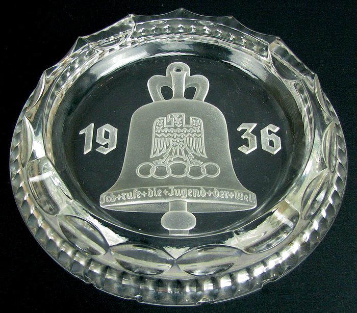 Glasaschenbecher 1936  | Glasaschenbecher mit geschliffener Olympischer Glocke mit Adler und dem Schriftzug „Ich rufe die Jugend der Welt“, "1936", 15,5x2,3 cm.