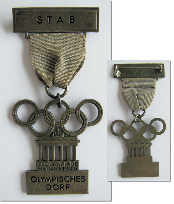 Teilnehmerabzeichen 1936  | Offizielles Teilnehmerabzeichen für Mitarbeiter der Leitung des Olympischen Dorfes mit Aufschrift "Olympisches Dorf" und zusätzlicher Plakette mit Aufdruck "Stab". Mit hellviolettem Seidenband. Hersteller: "L.Chr. Lauer, Nürnberg-Berlin". Bronze, versilbert, 8,8x4 cm.