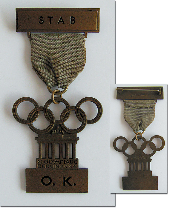  - Olympic Games 1936 : Official particiapation badge for a member of the administration of the Olympic Village, incribed "Olympisches Dorf" plus an additional badge "Stab" (staff). With mauve silk ribbon. Manufacturers "L.Chr.Lauer, Nürnberg-Berlin". Silver plated bronze,8.8 x 4 cm. Slik ribbon slightly shopworn. Condition: A-