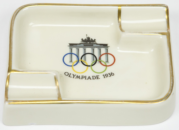  - Ashtray inscribed "Olympiade 1936," featuring the Brandenburg Gate and the Olympic Rings. Porcelain; manufacturer: Königszell; partially gilded. 12 x 9.5 x 2.3 cm. --Small chip on the outer rim of the base Condition: A-B