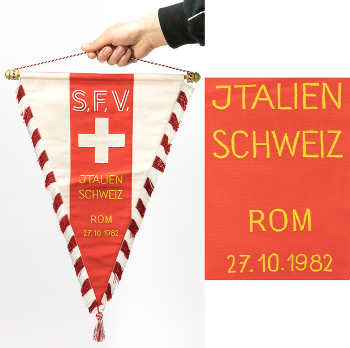  - Original match pennant of the Swiss national team from the football match between Italy and Switzerland on October 27, 1982, in Rome. Silk, embroidered. Features silk fringe, silk tassels, and a red-and-white looped ribbon. Gilded wooden crossbar with finials. 46.5 x 32 cm (excluding tassels). This match pennant was presented to Italy, the referees, and UEFA observers! From the collection of a UEFA observer. Condition: A-