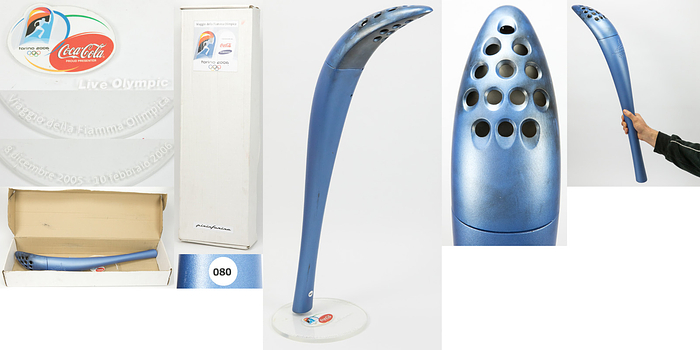 Olympiafackel 2006  | Original Olympiafackel der Olympische Spiele Turin 2006. Blaues technopolymer ummanteltes Aluminiumgehäuse, mit eingeprägtem Schriftzug "Torino 2006" dem Olympischen Logo und den Ringen. Höhe 77 cm. Hergestellt von Pininfarina. Mit der Trägernummer "080". Mit original Stoffsack und Promotionständer aus Plexiglas von Coca-Cola mit Inschrift. Dabei original Karton für Fackel und Ständer