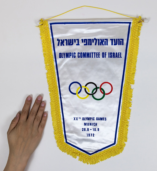  - Official team pennant of Israel for the Olympic Games Munich 1972. Colour printed, with silk fringes, wooden pole with plastic balls, 40x29 cm. On 5th September 1972, Palestinian terrorists attacked the Israeli team in the Olympic Village at the 1972 Olympic Games in Munich. Eleven members of the team and a policeman were killed. Condition: B