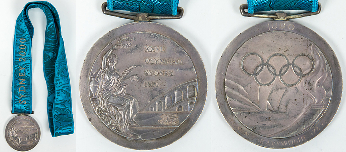  - Winner's medal for 2nd place in Women's Judo at the Sydney 2000 Olympic Games. Silver, engraved with "Judo" and "Women's Heavyweight +78 kg." With original embroidered silk ribbon. 6.8 cm. --Silver tarnished; with signs of wear. The buyer learns the name of the female athlete. Condition: A-