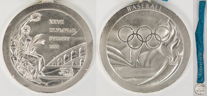  - Olympic Games Sydney 2000 Silver Winner Medal: Winner medal for the Baseball runner-up champion Cuba, second at the Olympic Games in Sydney 2000. Silver, engraved "Baseball" plus original silk ribbon which is embroidered, 6.8 cm. signs of wear, two small dents on edge. They occured at the party held by the Cuban Basball players after the award ceremony in Sydney. Silk ribbon loose Condition: A-