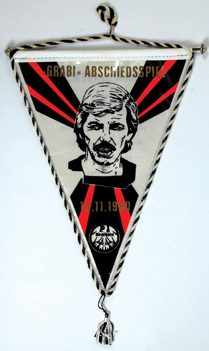 Frankfurt,Eintr.- Wimpel 1980  | Offizieller Wimpel vom Abschiedsspiel von Jürgen Grabowski mit goldenem Aufdruck "Grabi Abschiedsspiel 12.11.1980" und dem Porträt der Eintracht - Legende. Rot-schwarze Seidebordüre mit Bommel. Metallstange mit Kugeln. 28x20,5 cm (ohne Bommel).
