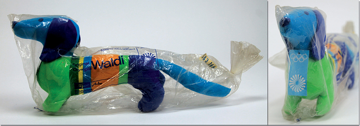  - Olympic Games Munich 1972. "Waldi", mascot made by „Hegi“ for the Olympic Games in Munich 1972 Colour cloth with tag at the neck. 33x15 cm. In original wrapping (with tears). Original mascot from 1972, no replica. Replicas have been on the market since approx. 2022 (these can be recognised by the Olympic Games logo embroidered on the body). Condition: A