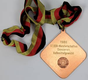  - Two winner's medals from the 1979 and 1980 East German Boxing Championships: 1) Gold medal inscribed "1979 East German Championship Senior Featherweight" with silk ribbon. 2) Bronze medal "1980 East German Championship Senior Light Middleweight" with silk ribbon. Each 8x8 cm in original box. Also included: an honorary plaque of the German Boxing Association (DBV) - East Germany with the inscription "Honorary Plaque Gerd Lang" on the reverse. Gilt bronze with an applied, enameled state coat of arms, 8.5x8.5 cm. --signs of usage Condition: B - Bild 5