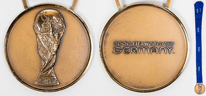 Siegermedaille WM2006  | Offizielle Siegermedaille der deutschen Mannschaft für den 3.Platz bei der Fußball-Weltmeisterschaft 2006 in Deutschland. "2006 FIFA World Cup Germany“ Bronze (51 Gramm) an original, blauem Seidenband. Hersteller: Bertoni. 6 cm. Diese Medaille kommt aus dem Nachlass des DFB-Physiotherapeuten Adolf Katzenmeier (1934-2016) der für die Nationalmannschaft von 1963-2008 tätig war.